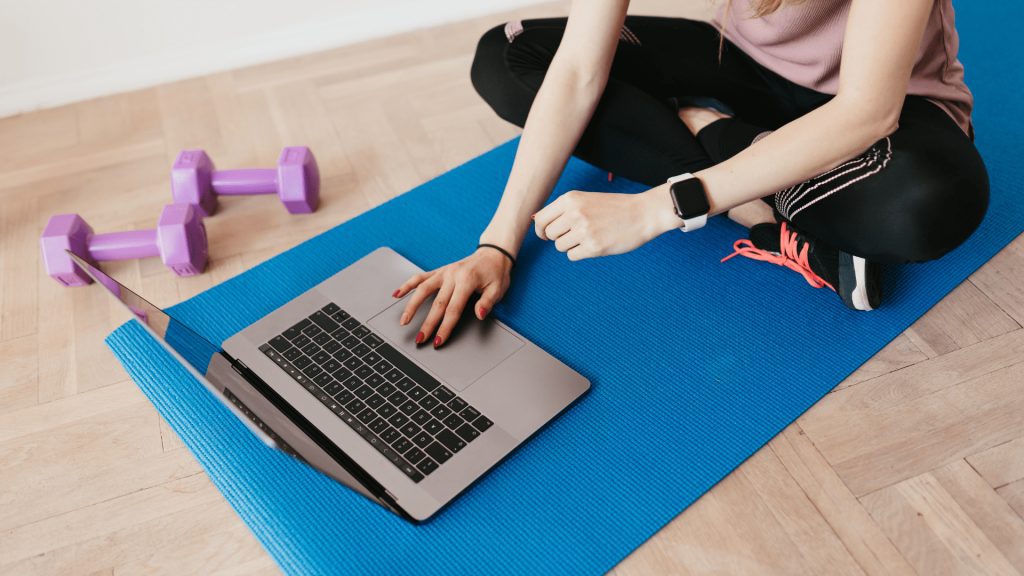 Female sitting on yoga mat touching apple Mac computer, Dumbells sitting around