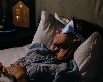 Lady Sleeping in a bed with a blue eye cover on, White Pillows